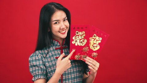 Asian woman in modern cheongsam costume holding shopping bags isolated on red studio background. Chinese new year in shopping concept style.chinese text mean goodluck.