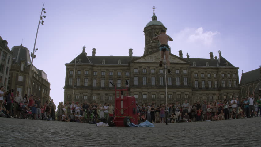 Amsterdam - March, 2012: Static shot of an acrobat juggling while balancing on a unicycle in front of a crowd of people in Dam Square near the town hall.