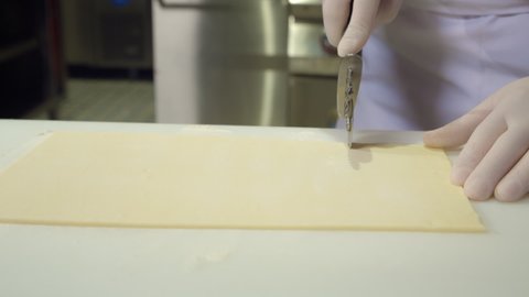 cutting dough, close up. cook cuts off part of raw dough sheet with a special dough knife. restaurant kitchen professional chefs work. gloved male hands prepare ingredient before baking