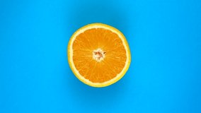 TOP VIEW: Half of an orange rotates on a blue surface - fast motion