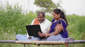 A middle-aged happy rural farmer couple sitting outdoors on an agricultural farm in traditional costumes and talking while using a laptop. Concept of Advancement in agriculture and technology  - Powered by Shutterstock - Get 15% off with code: PIKWIZARD15