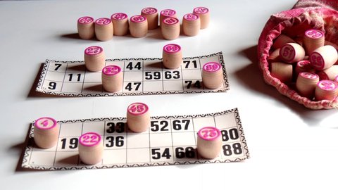 Traditional old Russian board game Russian Lotto. Cards with numbers, closeup. Wooden barrels with numbers and bag with barrels lie on table, on white background. hand in frame puts the keg video.