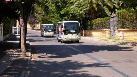 ISTANBUL - AUGUST 16, 2021: Small electric buses take tourists through green streets of Buyukada Island on a sunny day. New invention of environmentally-friendly public transport at popular place