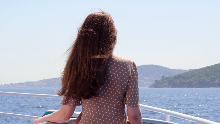 Woman stands at open deck of ferry ship, looking ahead to Princes' Islands. Tourist traveling through the sights of Istanbul on hot summer days. View from back, long hair fly in gusts of wind Royalty-Free Stock Footage #1085392724