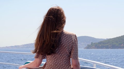 Woman stands at open deck of ferry ship, looking ahead to Princes' Islands. Tourist traveling through the sights of Istanbul on hot summer days. View from back, long hair fly in gusts of wind