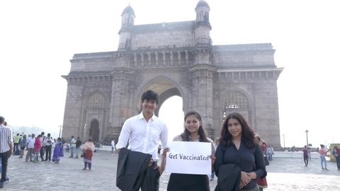 Mumbai - Maharashtra, India. January 15, 2022:A group of young  professionals holding up a sign "Get Vaccinated" in front of the Gateway of India in Mumbai, Maharashtra. Young professionals holding up