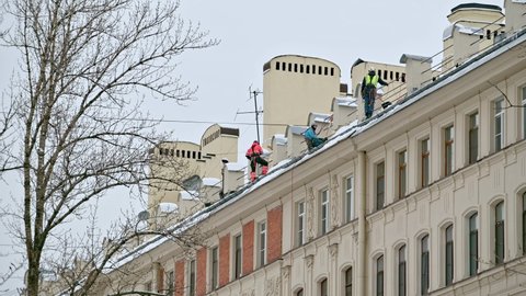 SAINT-PETERSBURG, RUSSIA - JANUARY 12 2022: 4K 16:9. Workmen from maintenance company clean living building roof from snow and ice, throwing them down