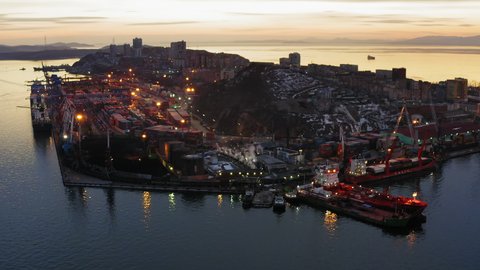 Drone view of the cargo terminal with port cranes at sunset. There are containers and cars on the quay. Freight shipping concept. Egersheld Peninsula, Vladivostok.