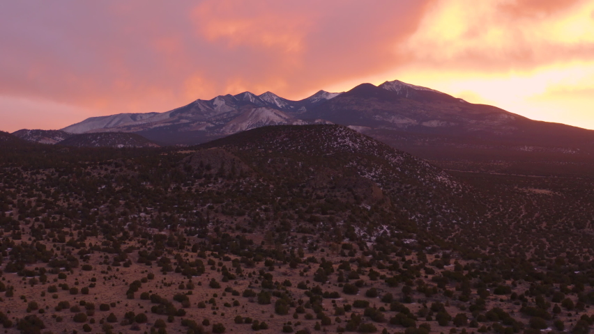 Beautiful aerial shot of the Coconino National Forest and San Francisco Peaks north of Flagstaff, Arizona seen at sunset. The sky is pink and orange. The camera makes a dolly in, pedestal up motion. Royalty-Free Stock Footage #1085413112
