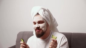 Portrait of funny man in white tshirt applying cucumber slices over clay mask on his face. Self care morning spa procedure - Powered by Shutterstock - Get 15% off with code: PIKWIZARD15