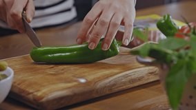Close-up hands of woman cutting green pepper on a wooden floor in the kitchen. Woman is cutting green pepper in the kitchen. Slicing green peppers to make sandwiches.