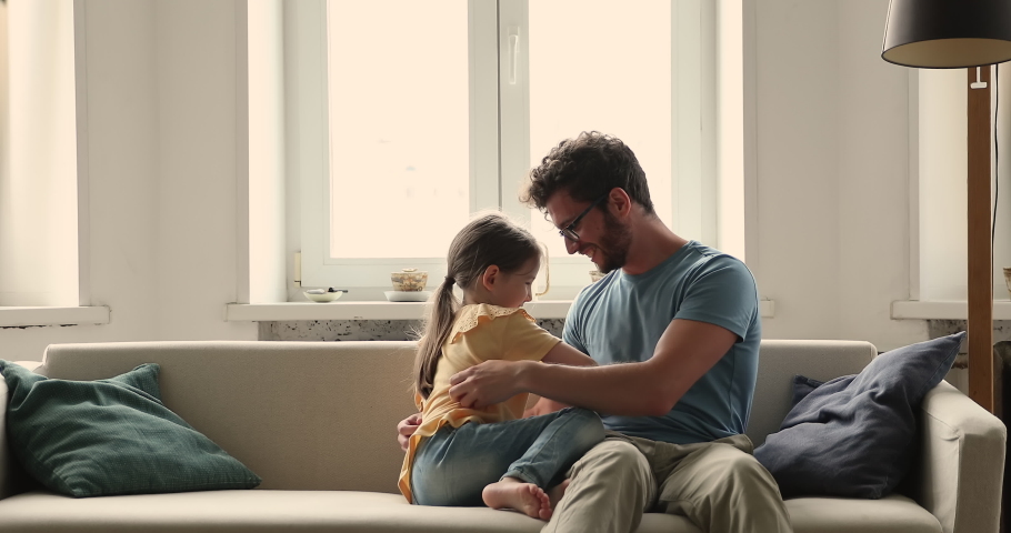Playtime of father and little daughter, fun concept. Young daddy sit on cozy sofa with child, loving family tickling each other playing at home, spend carefree weekend together feeling bond and love Royalty-Free Stock Footage #1085422379