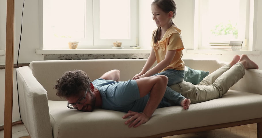 Little 5s girl sits rides on daddy back play together at home. Young loving father lying on cozy couch in living room enjoy playtime with adorable preschool daughter. Family bond, funny games concept Royalty-Free Stock Footage #1085422382