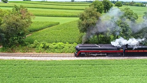 Ronks , Pennsylvania , United States - 07 24 2021: Ronks, Pennsylvania, July 2021 - An Aerial View of Amish Farm lands With a Single Rail Road Track and a Steam Passenger Train Approaching