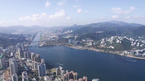 High skyscrapers at Vista Paradiso and big appartments in the background between the mountains of Tai Po Kau and Shing mun river on a cloudy and sunny day. Wide angle drone lowering shot