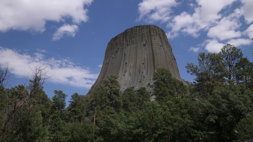 Upward, close steady shot of the Devils Tower, with beautiful clouds in the skies. 