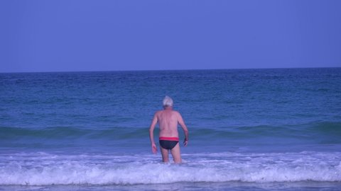 Senior man entering the sea with ocean waves