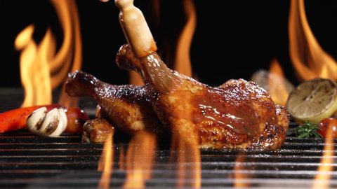 Chicken thighs grilled on hot barbecue charcoal flaming grill with sauce brushed on top. Juicy chicken meat roasted on bbq grill. slow motion