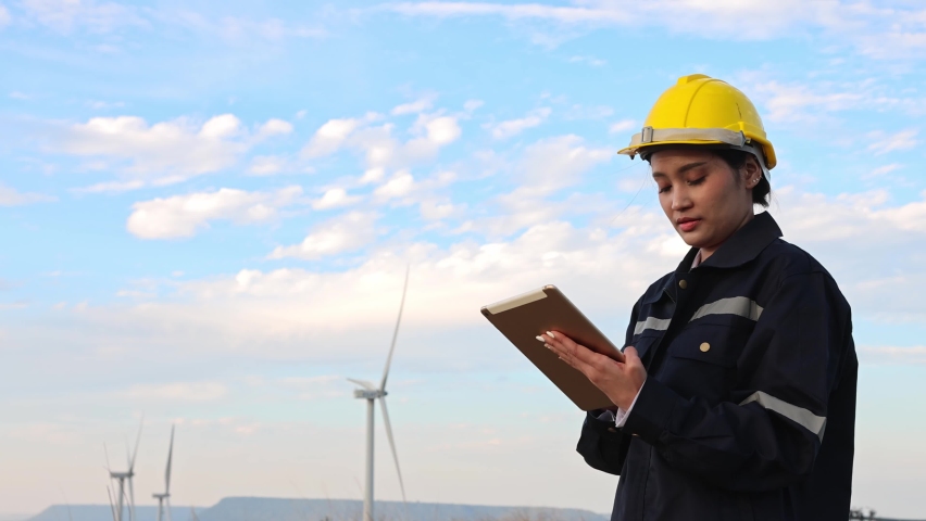An engineer analysis at a wind turbine and holds a tablet in her hands. | Shutterstock HD Video #1085428889