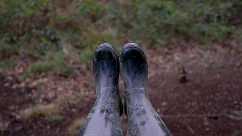 First person view as they enjoy a swing in a woodland setting. Persons wellington boots shown moving up into the air above the tree tops and sky. Slow motion footage of person out in nature.