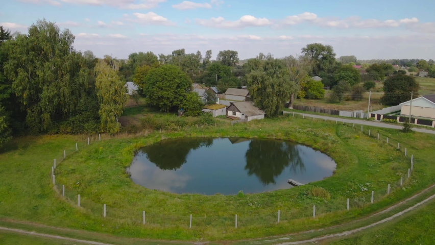 Small pond in the village against the background of old houses. Drone flight around the lake, 4K video