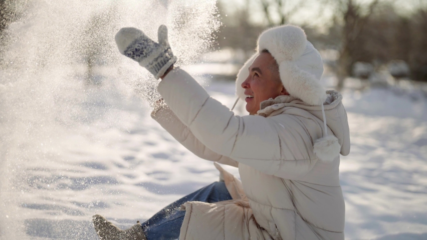 A gay gay man in warm clothes sits in the snow in winter and plays and enjoys a sunny day.