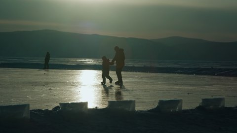 Father and son go ice skating on a frozen lake at sunset in winter