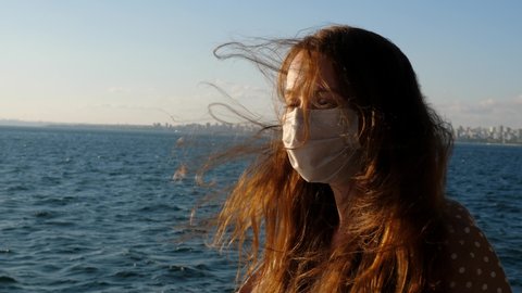 Warm wind ruffled the woman's long hair, tourist wearing a medical mask while traveling on an Istanbul ferry. She is sailing at Marmara Sea from the Prince Islands back to city