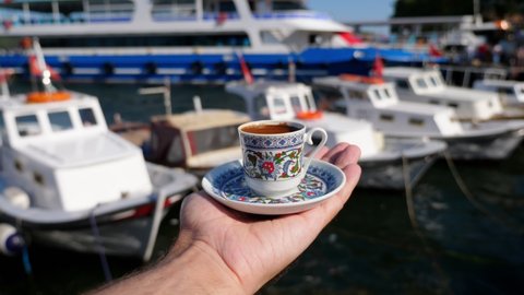 Tourist man enjoying his vacation on the islands of Istanbul stands on the waterfront with a cup of coffee. Fishing boats bobbing in the water along the shore. Man hold cup of Turkish coffee in hand