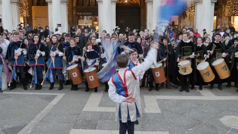 Venice, Italy FEBRUARY, 18, 2017 Young flag-wavers Caucasian male teen perform at the Venice Carnival with a group of drummers in the background surrounded by the amused audience