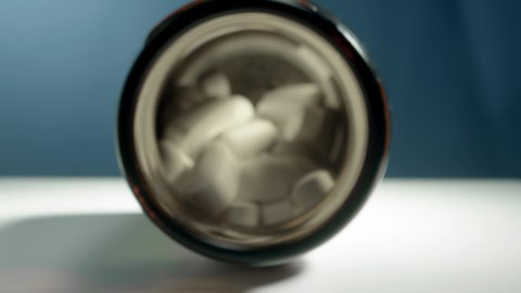 white pills in jar, dolly in slow inside jar. bottle of medicine lies on table on blue background, extreme macro footage of white matte drugs, penetrating movement.