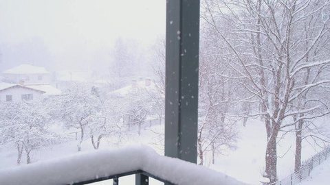Heavy snowfall in small town. Fluffy snowflakes tumbling down on the balcony. Blizzard in residential area with low-rise buildings. Winter view of countryside with snow covered trees and houses