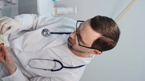 Male doctor putting medical glove. Vertical video portrait. Man in eyeglasses at spa salon. Prepare to treatment procedure. Hygiene virus protect