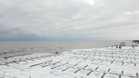 Aerial view over Lake Michigan boat marina.  Water inland is frozen with ice floes farther out. Cloudy sky. Snow covering the ice. 