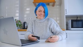Happy white woman buying online. Individual Caucasian female with dyed blue hair shopping at home with credit card and mobile phone. Cheerful person purchasing in internet store with smartphone