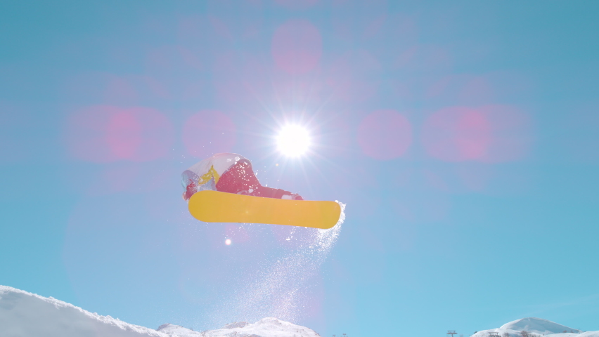 SLOW MOTION, BOTTOM UP, LENS FLARE: Golden sunbeams shine on an extreme snowboarder doing a spinning grab trick while riding in ski resort snowpark. Male tourist doing tricks while snowboarding. | Shutterstock HD Video #1085453036