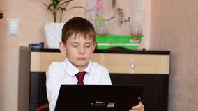 The theme of homeschooling children. Caucasian boy 7 years old sitting at home in front of the gadget pulls his hand to answer the question of the teacher. Teaching students at a distance.