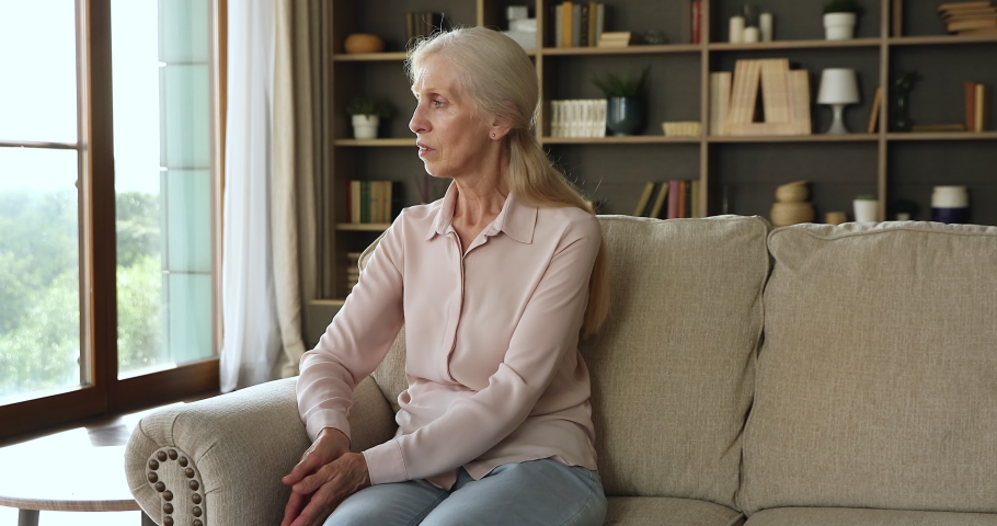 Pensive older hoary woman look into distance resting on sofa indoor, thinks about loneliness, reminiscing sits alone at home. Retirement, downhill of life, personal troubles and nostalgic mood concept | Shutterstock HD Video #1085456237
