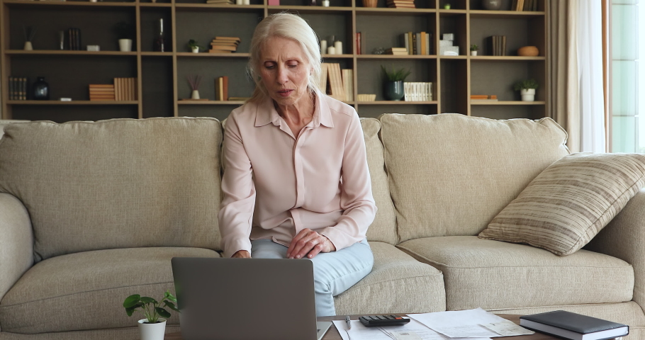 Frustrated mature woman sit on couch calculate expenses, review e-bank statement, feels stressed due lack of finances pay utility household bills, has bank debt, not enough pension for living concept Royalty-Free Stock Footage #1085456675