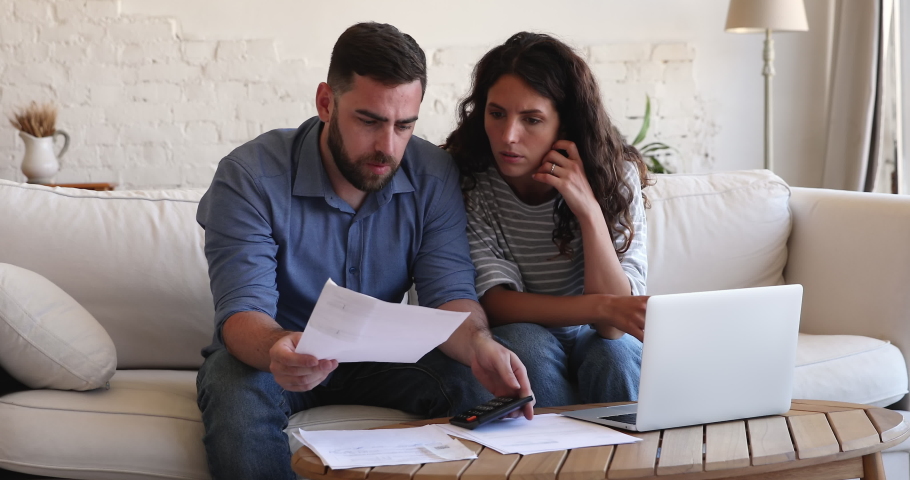 Couple sit on couch at table with laptop pay bills, use calculator count expenses, make budget control, manage finances, review overdue loan payments feel stressed. Crisis, lack of money, debt concept | Shutterstock HD Video #1085456708