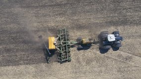video of a drone flying over a tractor with a harrow system, plowing land on a farm field, sunny weather. soil preparation for planting new crop, agriculture concept, top view. plant wheat