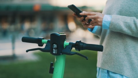 Woman using app on smartphone to unlock electric scooter on the street.