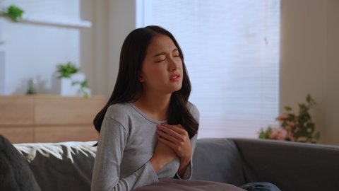Charming asian woman painning form chest pain, Trouble breathing. Female has difficulty breathing or pain in chest touches chest with her hand. heart disease or leaky heart valve concept.