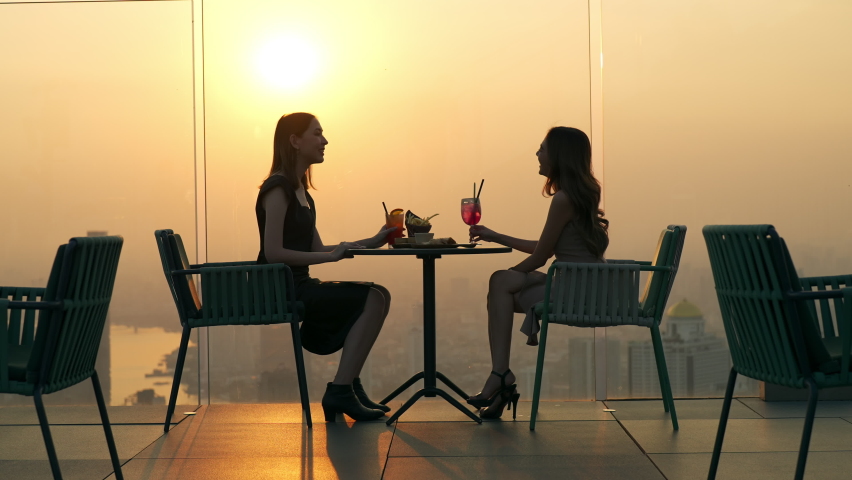 4K Young Asian woman friends celebrating dinner party meeting at skyscraper rooftop restaurant bar in metropolis at summer sunset. Beautiful girl enjoy outdoor lifestyle together on holiday vacation. Royalty-Free Stock Footage #1085470418