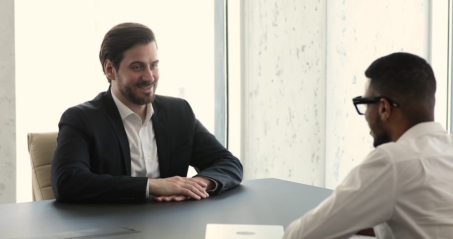 Confident millennial 35s man in suit sits at table in front of African HR manager, answers questions during job interview in company board room. Staffing, business negotiations, formal meeting concept Royalty-Free Stock Footage #1085474753