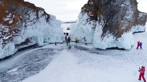 Aerial view on the rocky ice covered island in lake Baikal. Groups of tourist walking around on the cracked ice. Famous tourist spot. Beautiful winter landscape of lake Baikal