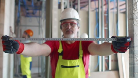 Portrait of mature builder using measuring tape at construction site. Realtime. 