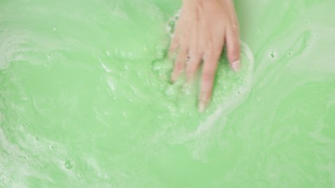 Hands mixing paints close-up, dissolved bath bomb. Decorative cosmetic products for bathroom concept. Liquid boiling texture. Spa procedure.