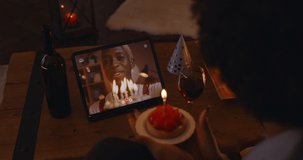 View from shoulder of african woman chatting with her boyfriend through video call and blowing candles on birthday cake. Concept of people, technology and virtual party.