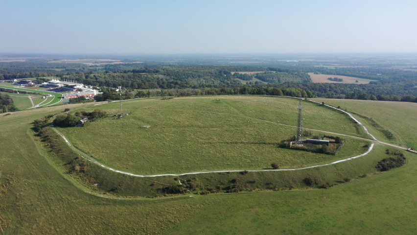 Pylons on a large mound at the top of a hill, horse racecourse and trees in background